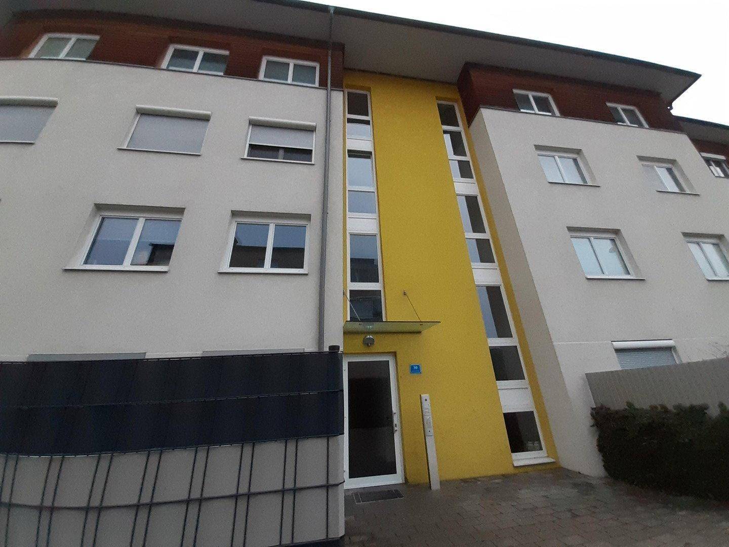 Moderne Gebäudefassade mit gelbem Akzent und großen Fenstern.