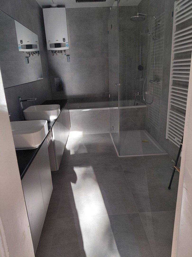 Modernes Badezimmer mit Doppelwaschbecken, großer Dusche und Badewanne in Grautönen.