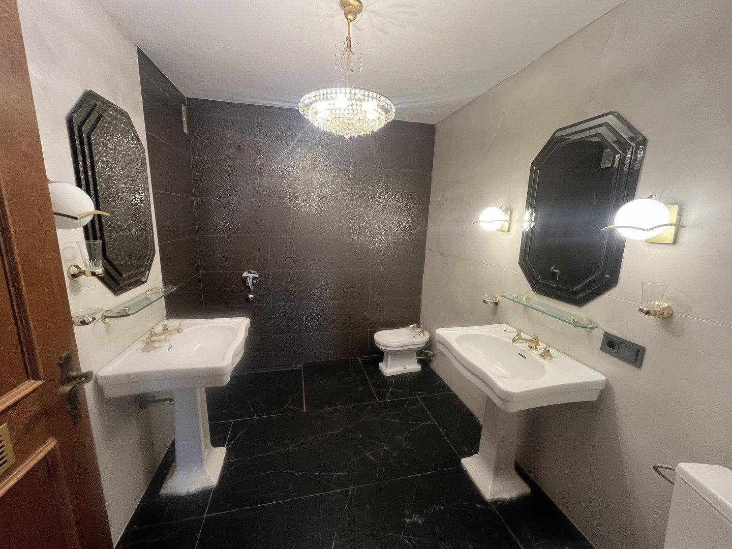 Elegantes Badezimmer mit zwei Waschbecken, dunklen Fliesen und einem dekorativen Kronleuchter.