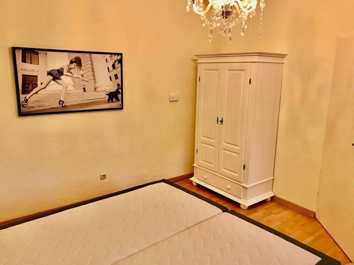 Schlafzimmer mit Bett, weißem Kleiderschrank und dekorativem Wandbild.