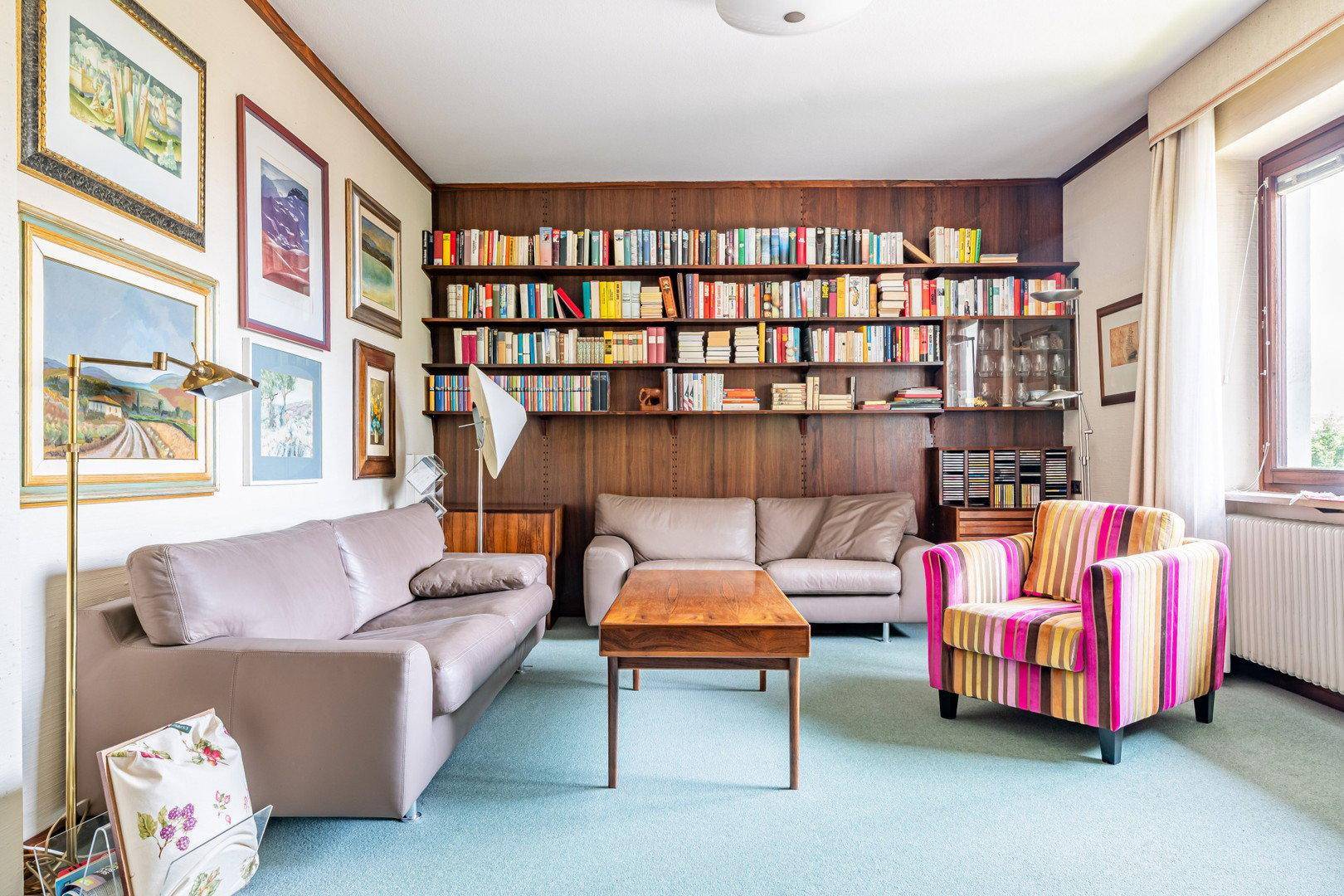 Gemütliches Arbeitszimmer mit großer Bücherwand, bequemen Sofas und Teppichboden.