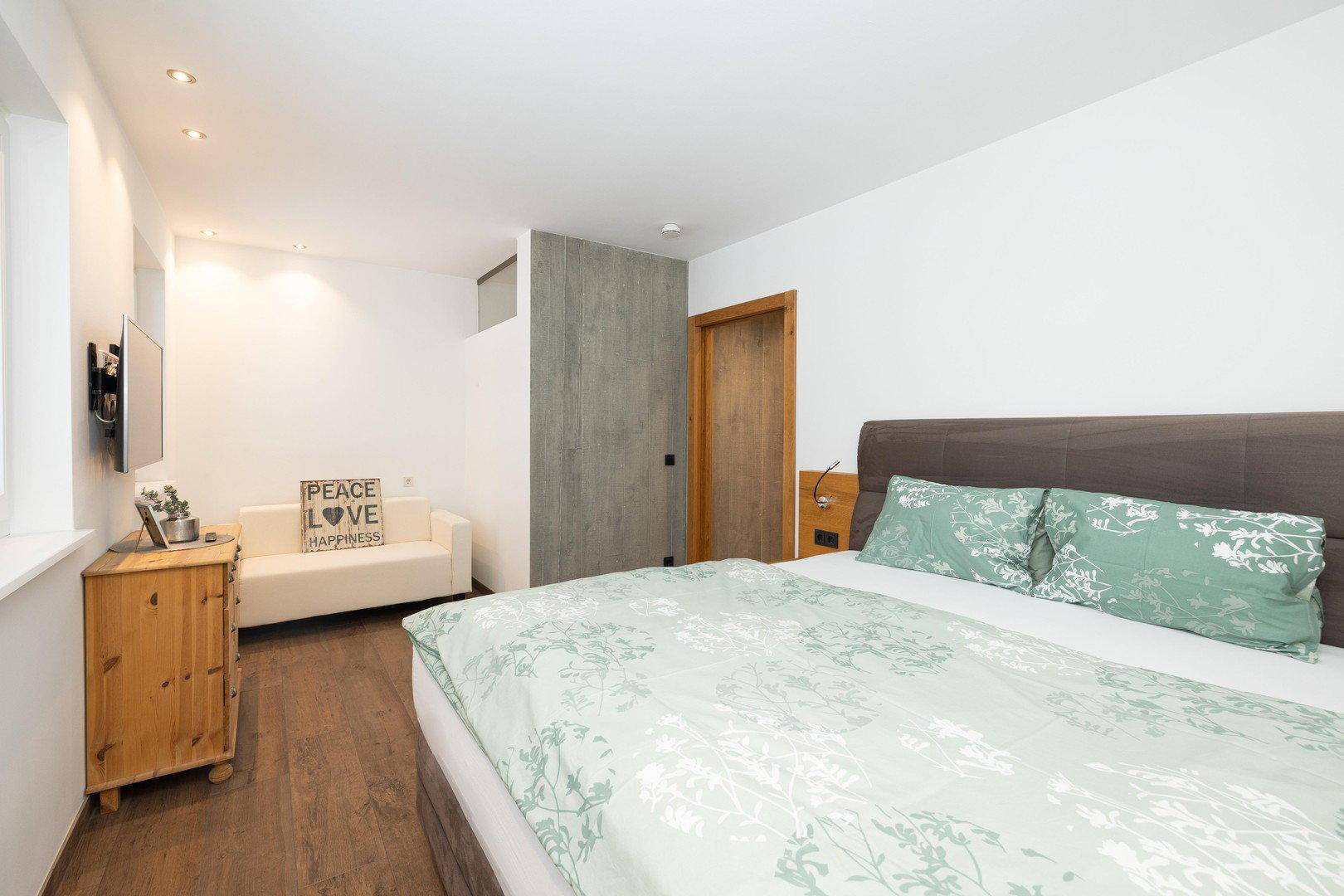 Modernes Schlafzimmer mit Doppelbett, Holzboden und einer kleinen Sitzecke.