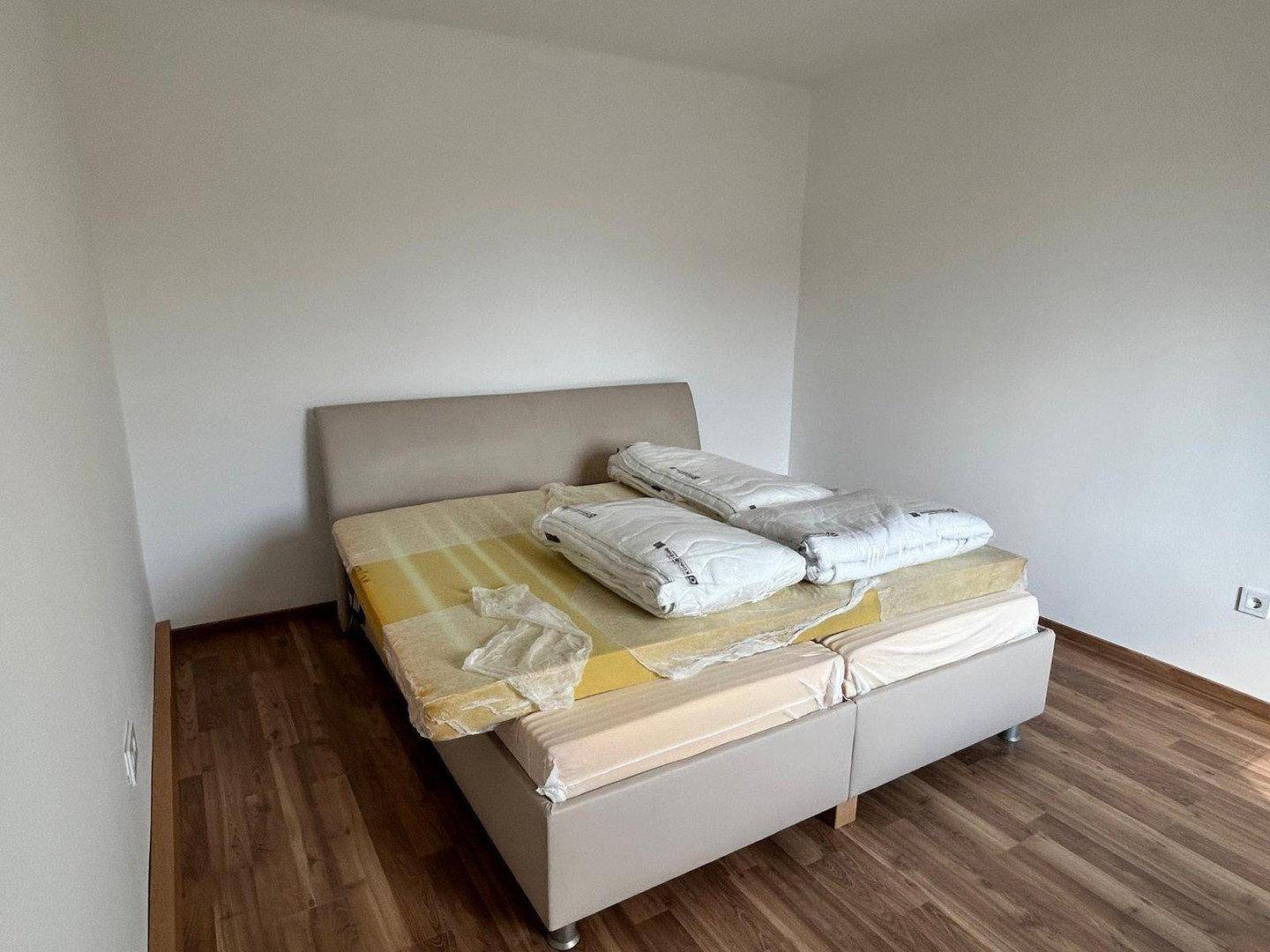 Schlafzimmer mit hellem Laminatboden und einem Doppelbett, bereit zur Einrichtung.