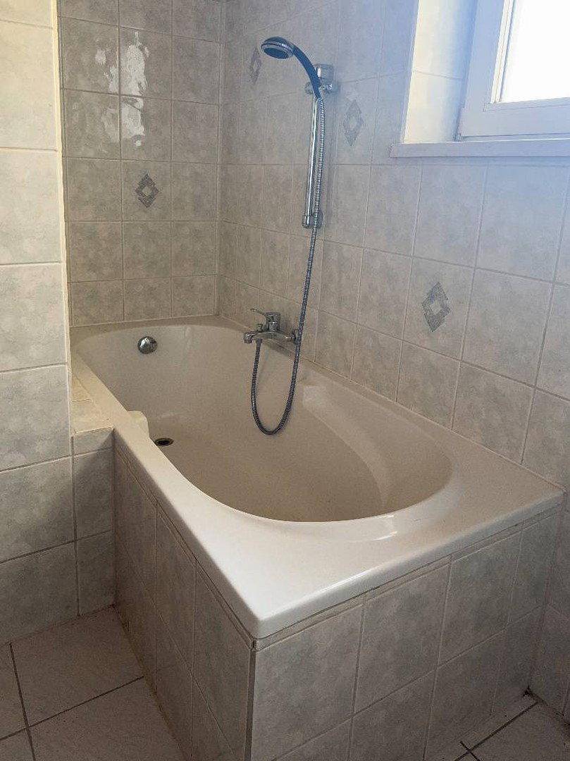 Eingebaute Badewanne mit Duscharmatur und hellen Fliesen im Badezimmer.