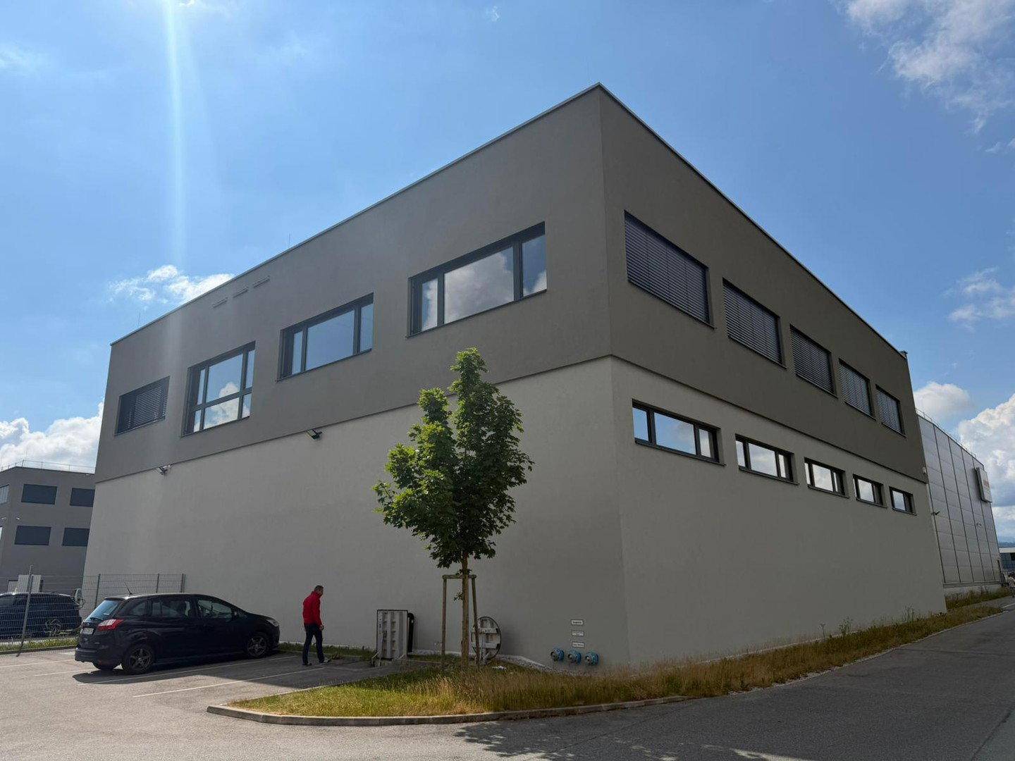 Seitenansicht eines modernen Geschäftsgebäudes mit Parkplätzen und grüner Umgebung.