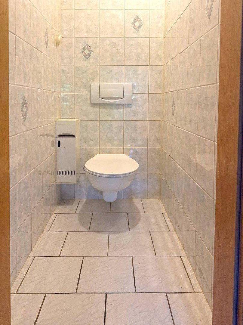 Separate Toilette mit Wand-WC und hellen Fliesen an Wänden und Boden.