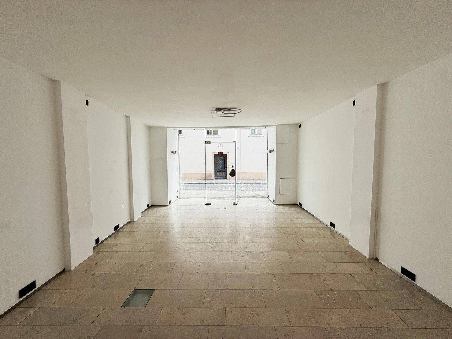 Geräumiger, leerer Geschäftsraum mit Fliesenboden und großer Glasfront zur Straße hin.