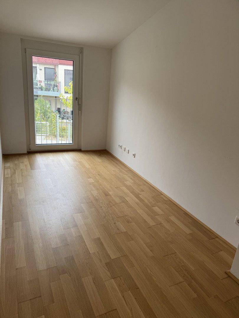 Geräumiges Zimmer mit Holzfußboden und französischem Balkon, der einen Blick ins Grüne ermöglicht.