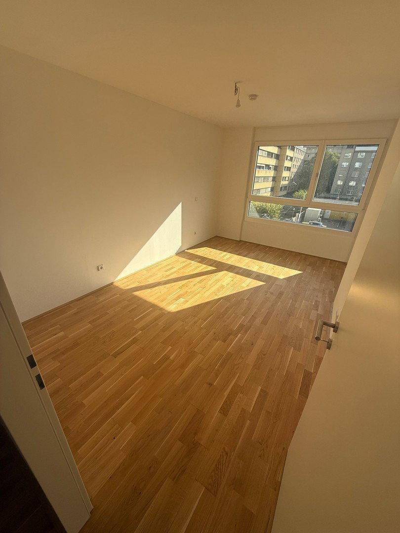 Helles Schlafzimmer mit Parkettboden und großen Fenstern, die viel Sonnenlicht hereinlassen.