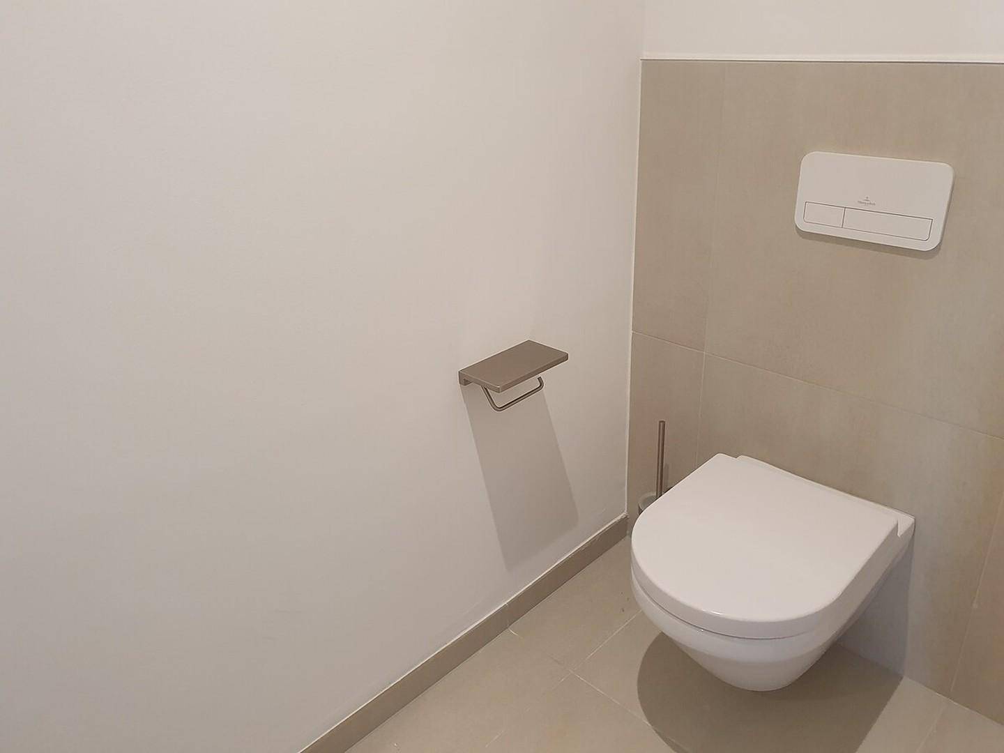 Separates WC mit wandhängender Toilette und hellgrauen Fliesen an der Wand.