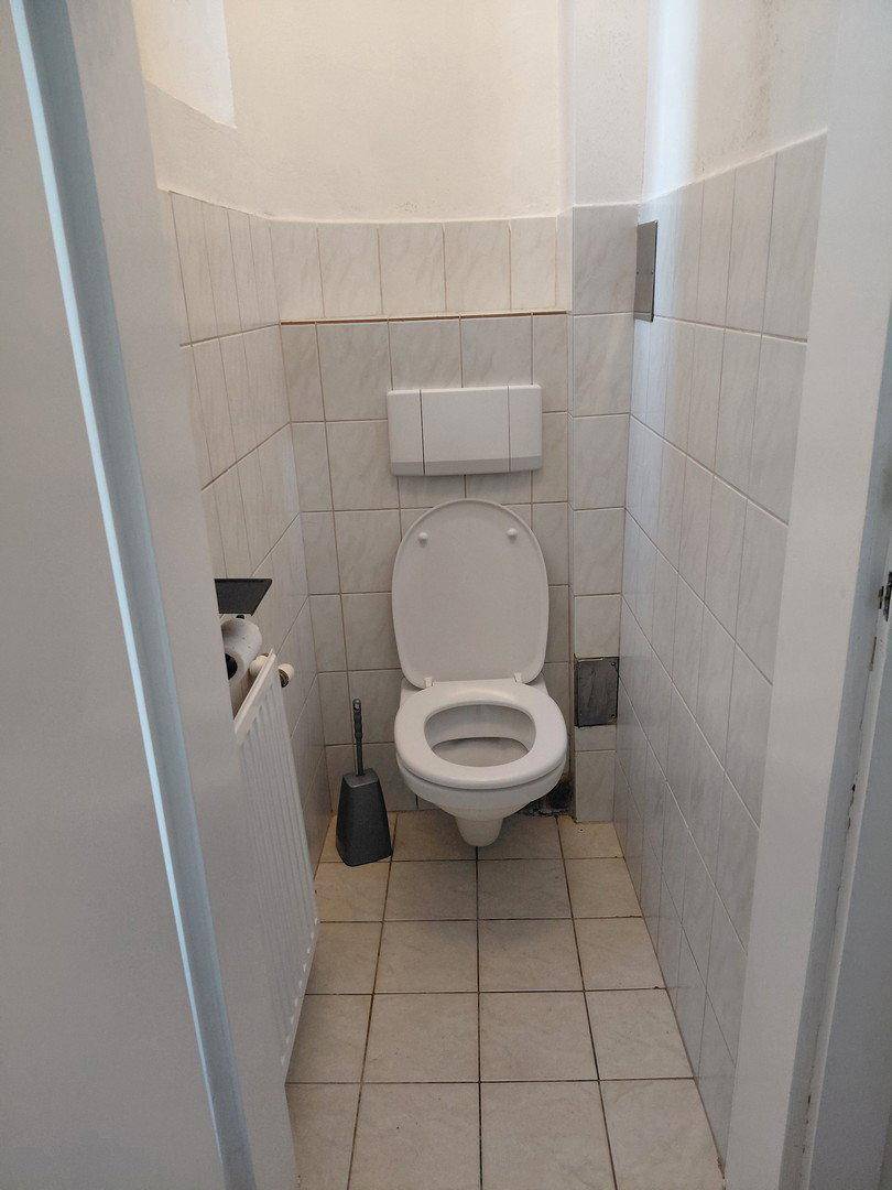 Kleines WC mit weißen Fliesen an Wänden und Boden, ausgestattet mit Toilette und Heizkörper.
