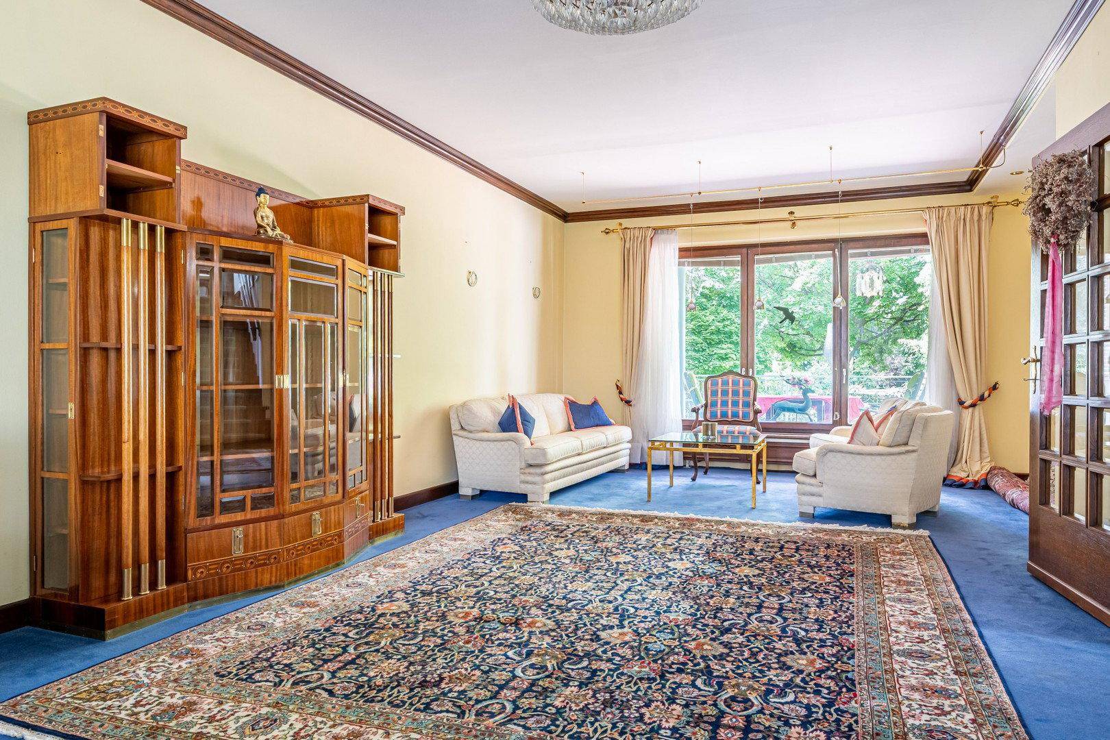 Geräumiges Wohnzimmer mit blauem Teppichboden, eleganten Möbeln und großem Fenster.