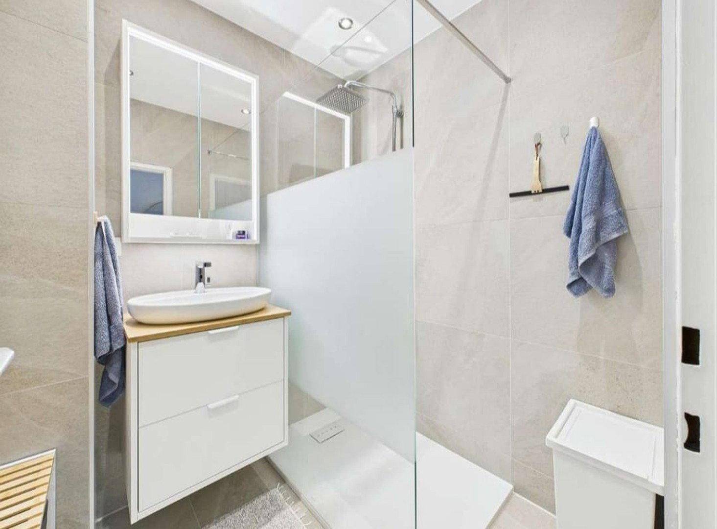 Modernes Badezimmer mit begehbarer Dusche, Einzelwaschbecken und hellen Fliesen.