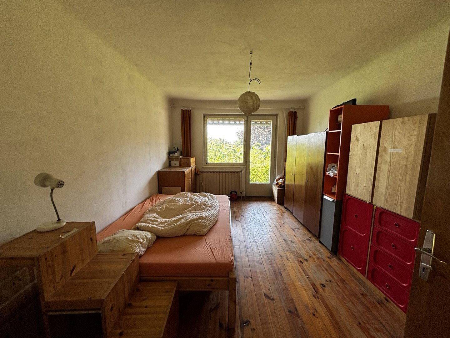 Schlafzimmer mit Holzboden, Einzelbett und farbenfrohen Aufbewahrungsmöbeln.