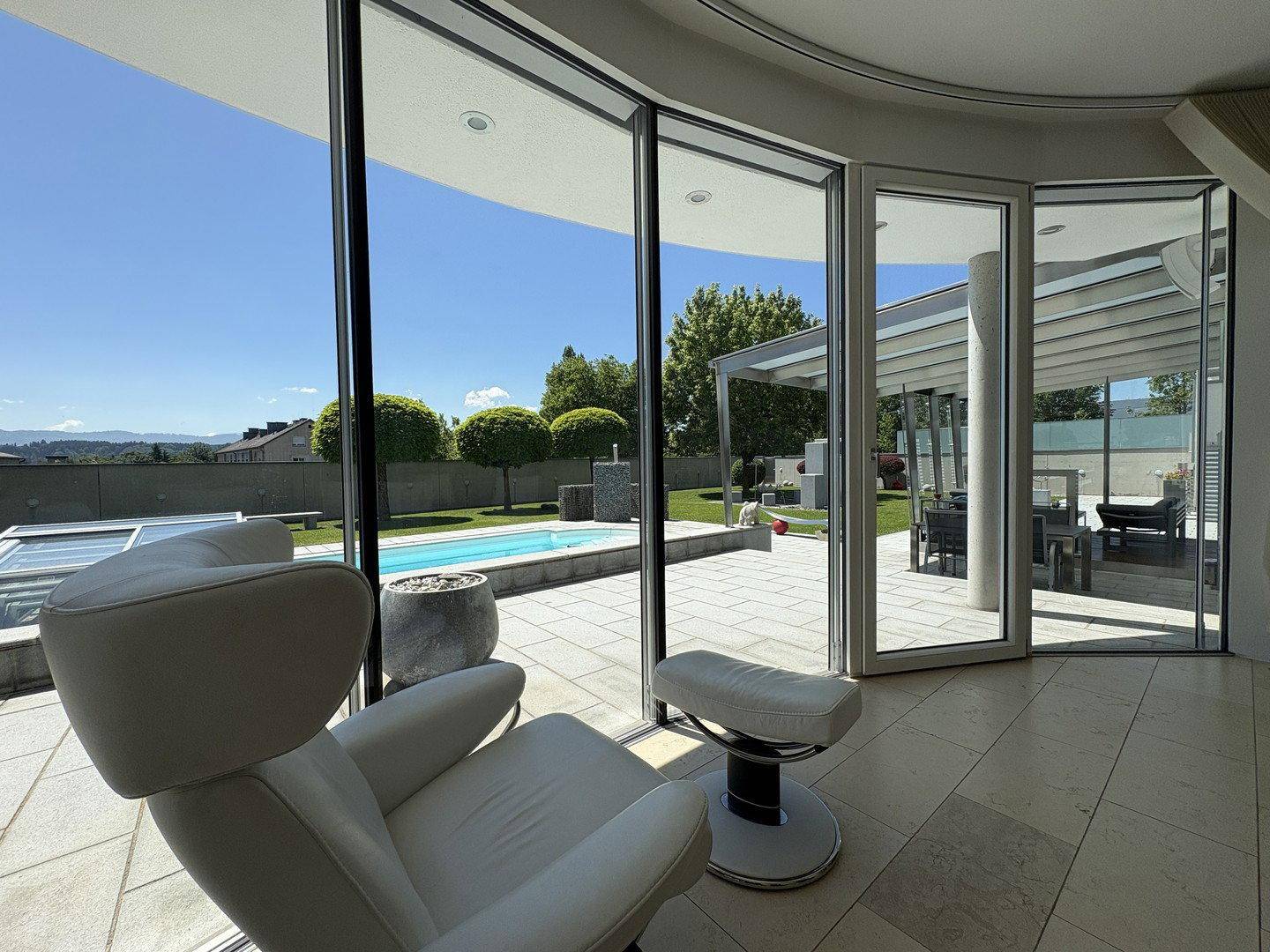 Lichtdurchfluteter Innenraum mit großen Glasfronten und direktem Blick auf den Pool und die Gartenlandschaft.