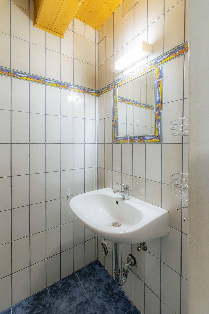 Kleines Badezimmer mit weißen Wandfliesen, blauem Boden und einem einzelnen Waschbecken.