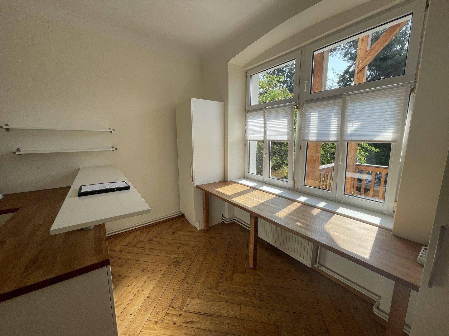 Heller Küchenbereich mit Holzarbeitsplatte, offenen Regalen und einem großen Fenster mit Blick ins Grüne.