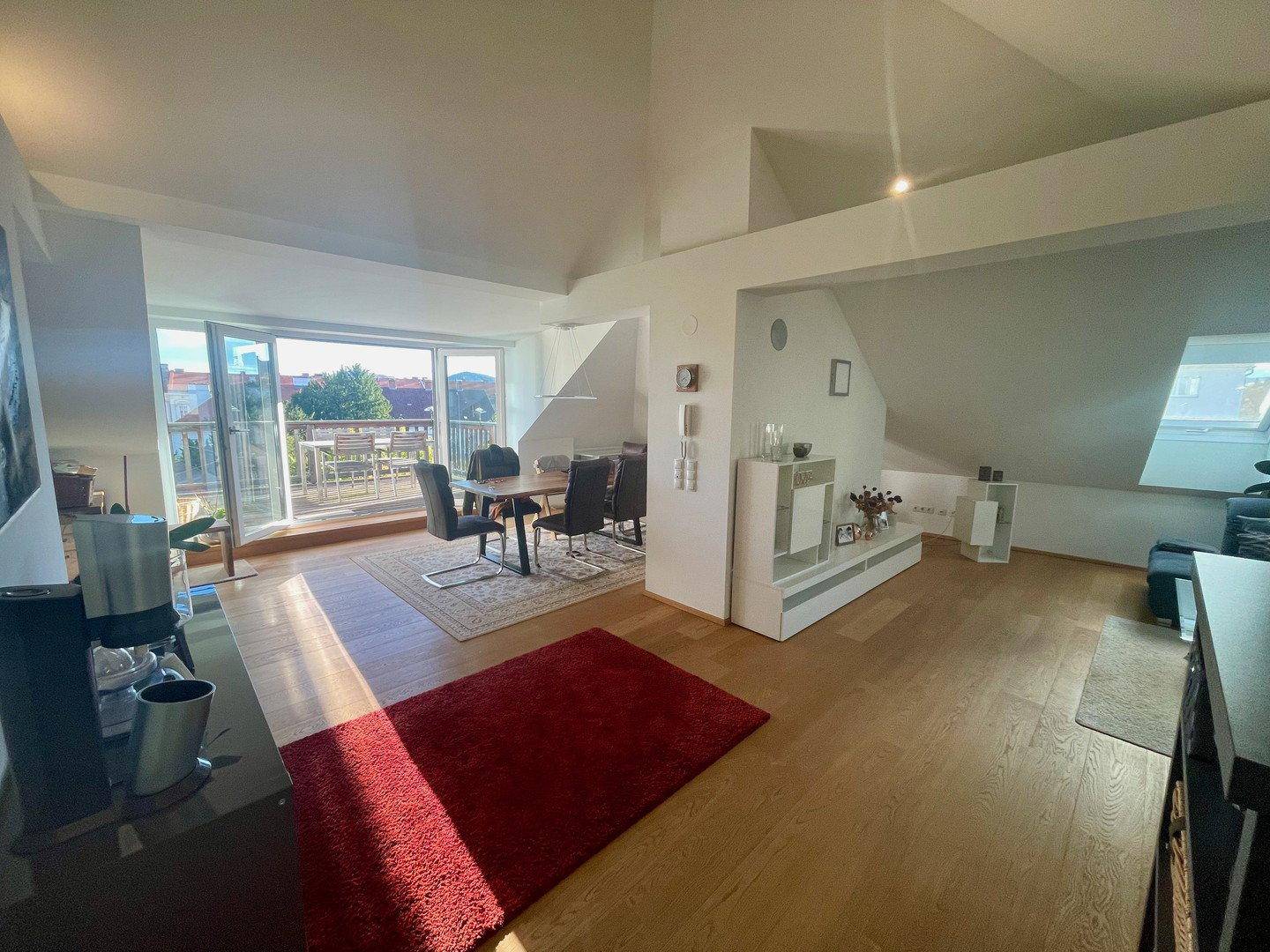 Heller, offener Wohn- und Essbereich mit Holzboden und Zugang zu einem Balkon.