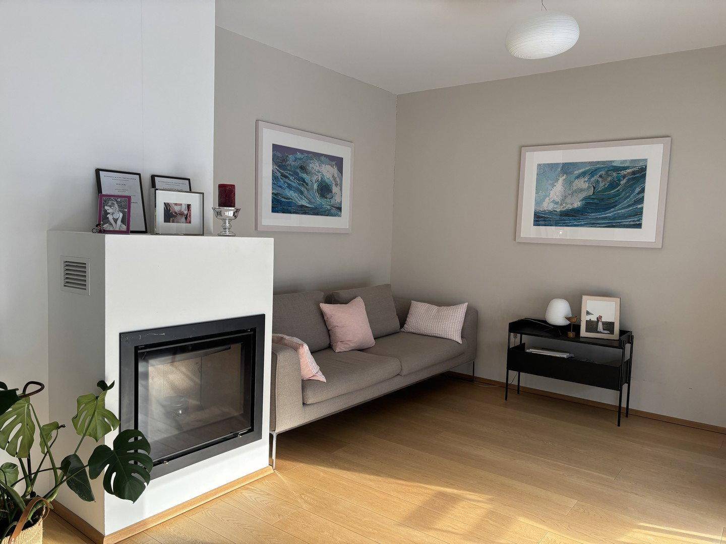 Helles Wohnzimmer mit modernem Kamin, beigem Sofa und Holzboden.