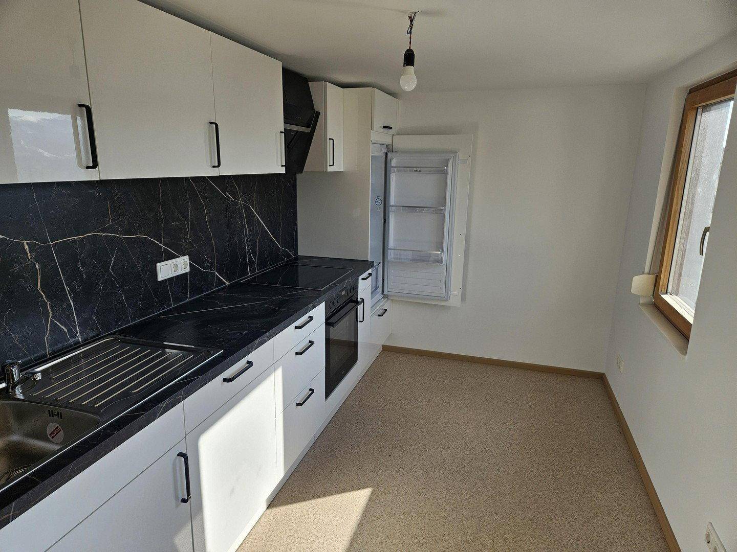 Neue Einbauküche mit weißen Schränken, schwarzer Arbeitsplatte und integrierten Geräten.