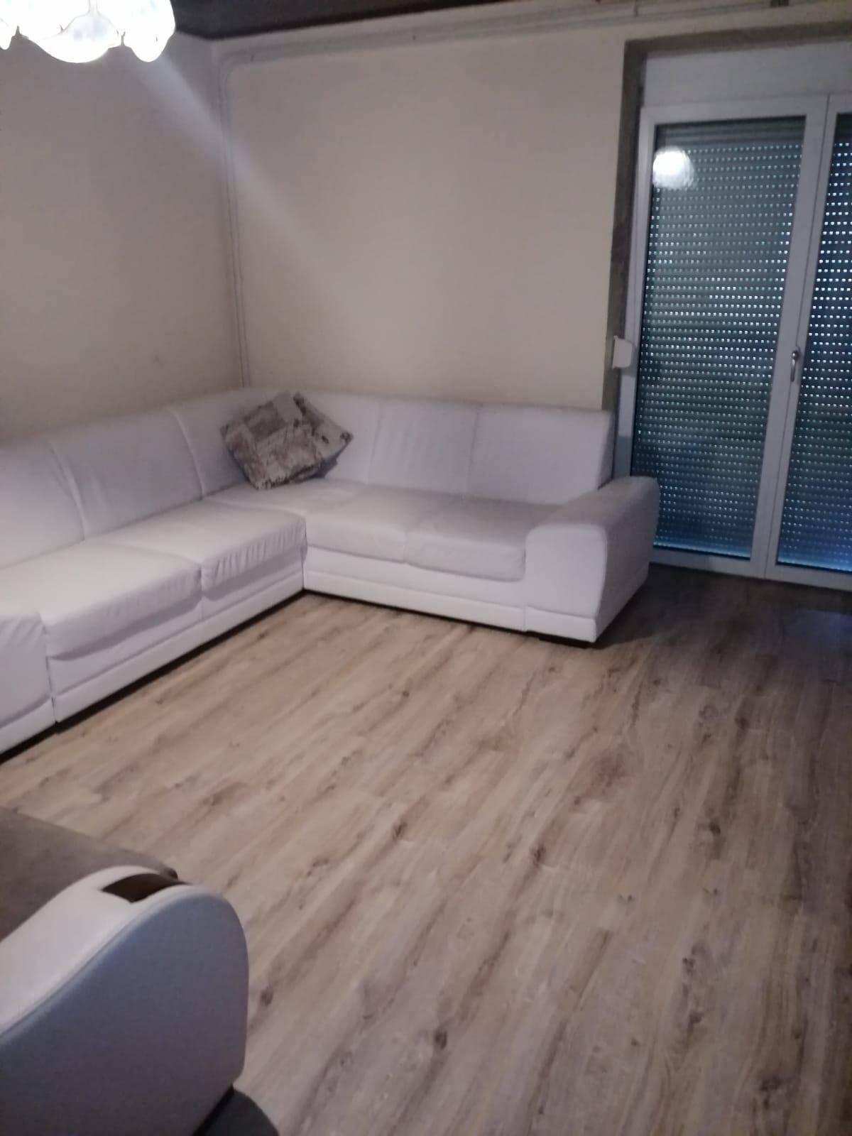 Helles Wohnzimmer mit weißem Ecksofa und Laminatboden.