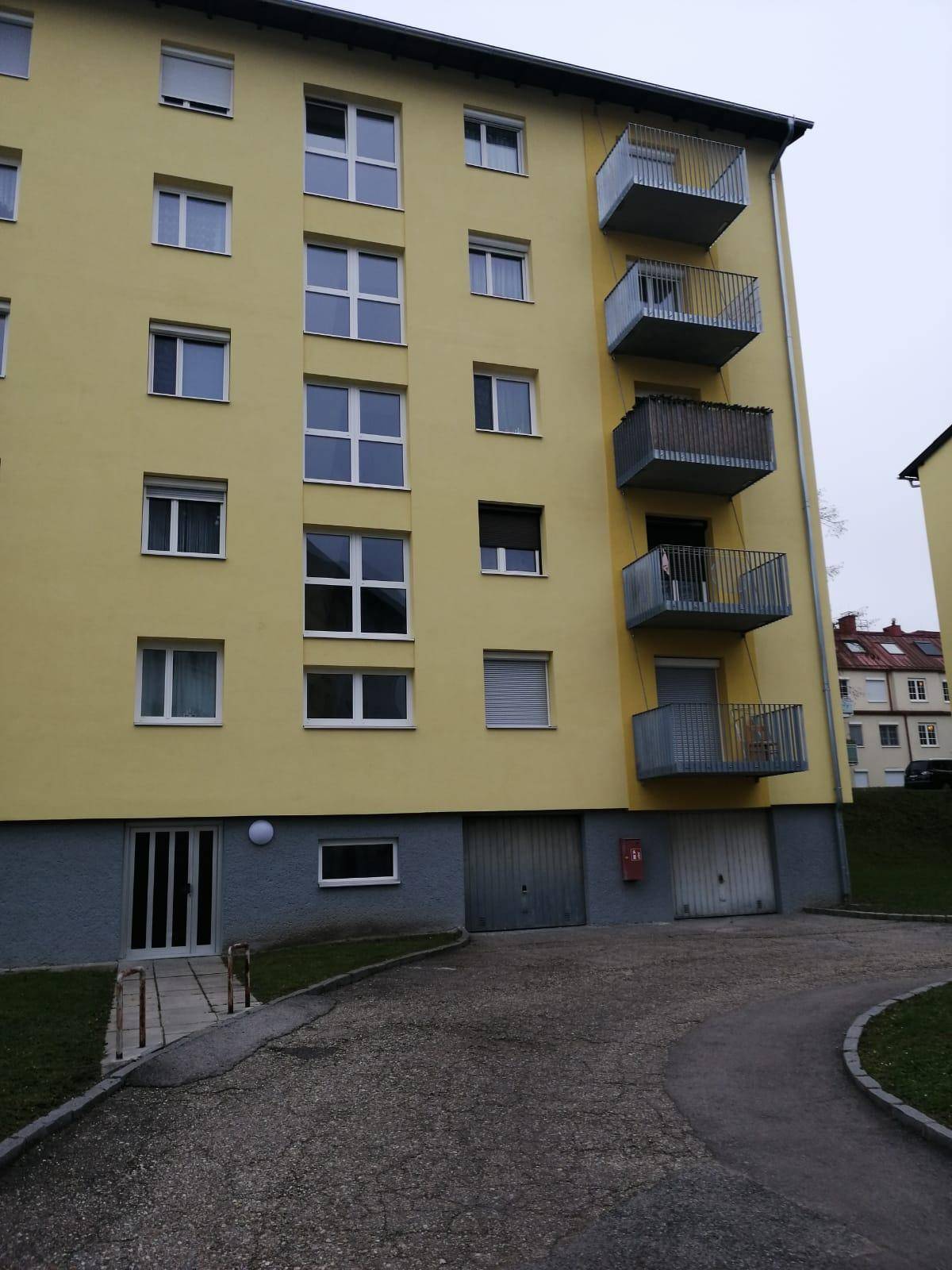 Gelbes Mehrfamilienhaus mit Balkonen und Garagen im Erdgeschoss.