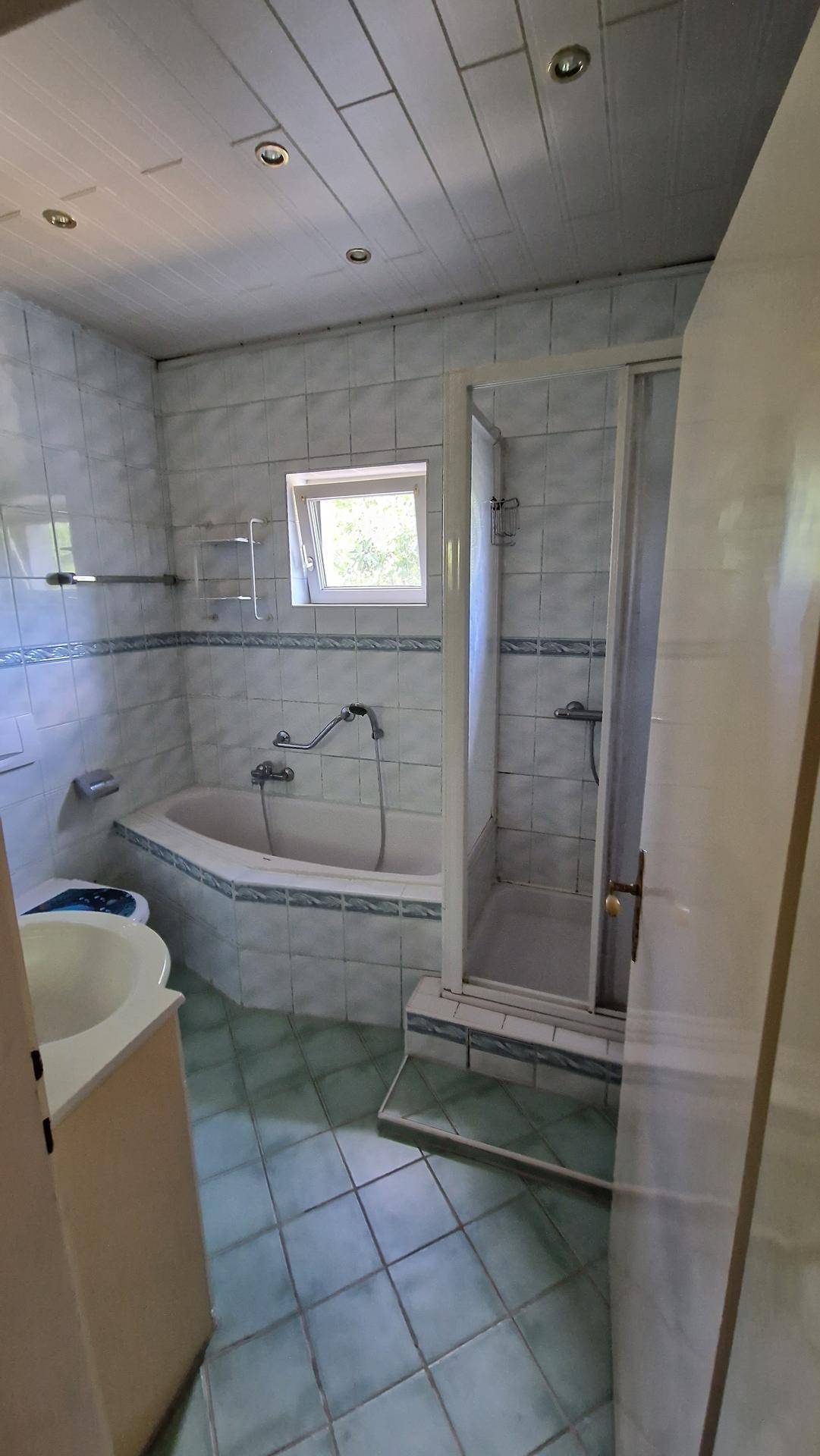 Badezimmer mit Badewanne, Duschkabine, Fenster und hellblauen Fliesen.