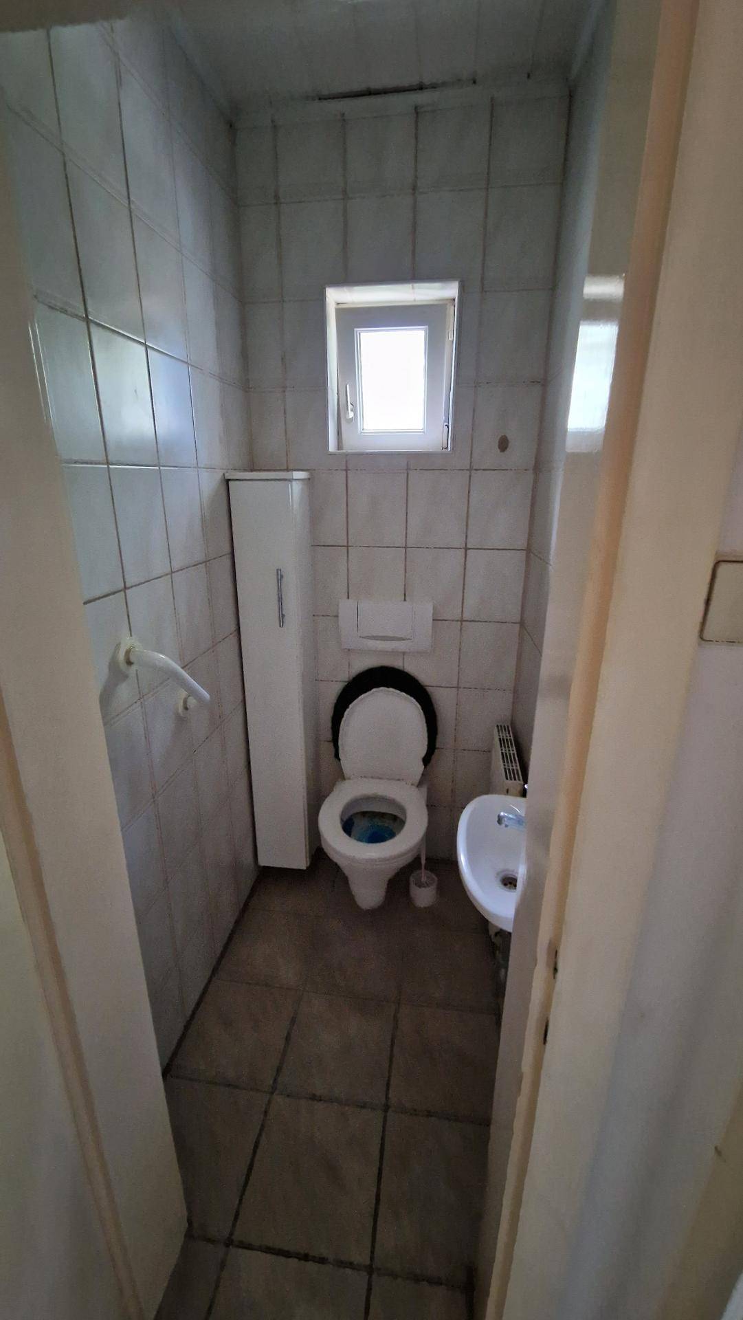 Kleines Gäste-WC mit Fliesen an Wänden und Boden sowie einem Fenster.