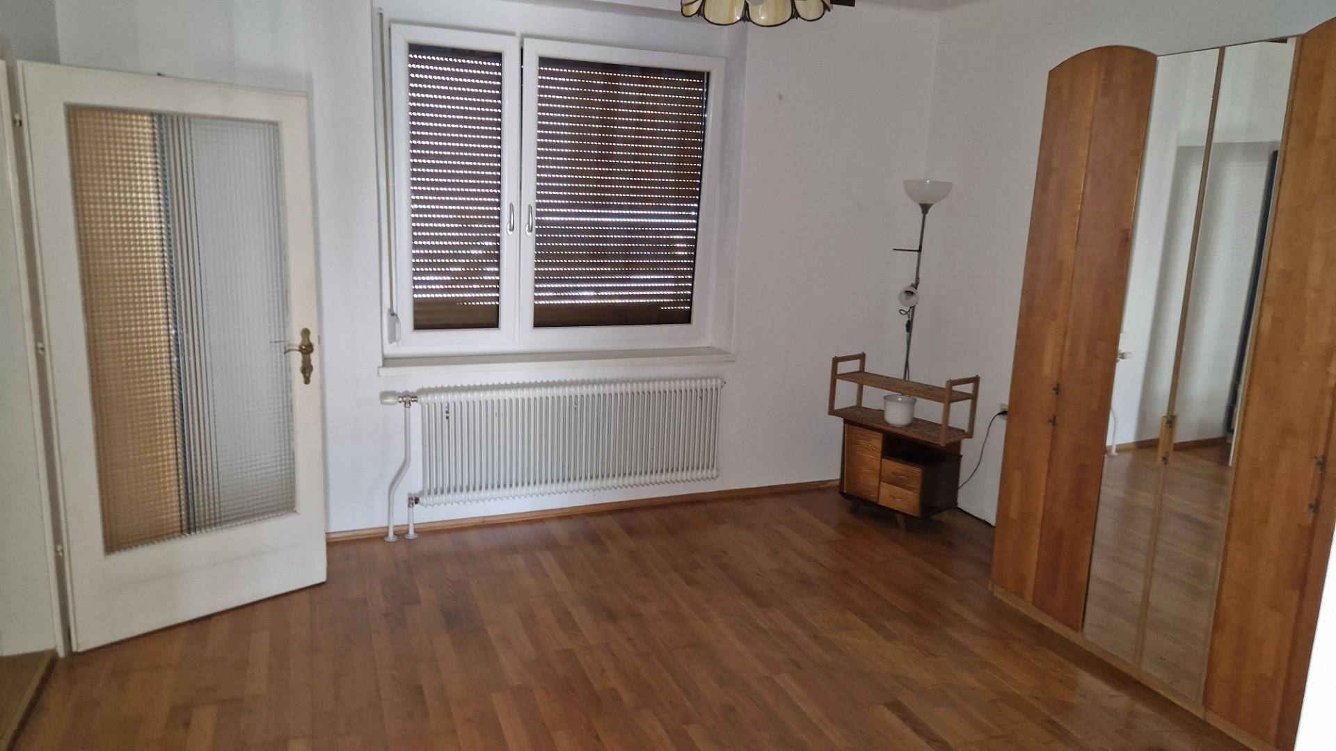 Zimmer mit Parkettboden, großem Spiegelschrank und einem Fenster mit Rollladen.