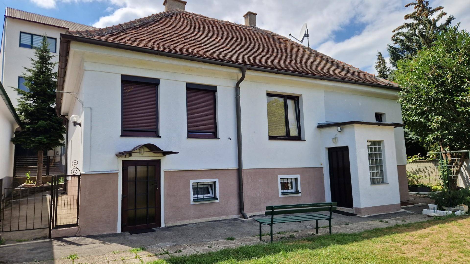 Seitenansicht des Hauses mit einem kleinen Gartenbereich und einer Bank vor dem Eingang.