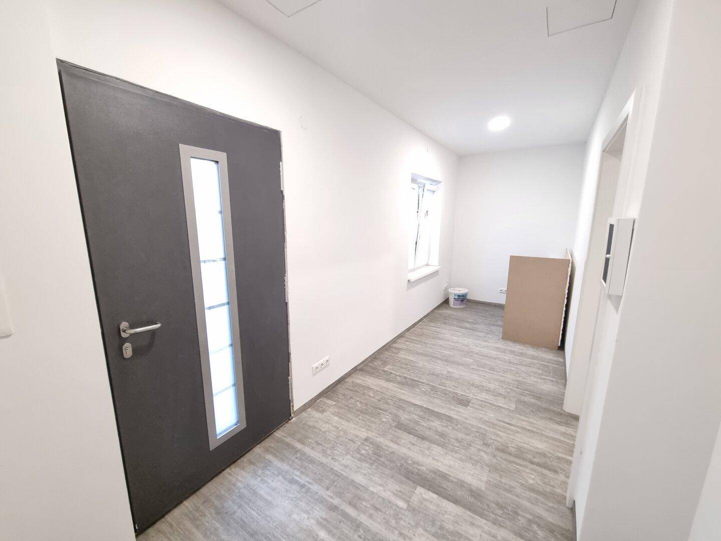 Eingangsbereich oder Flur mit dunkler Tür, kleinem Fenster und modernem Bodenbelag.