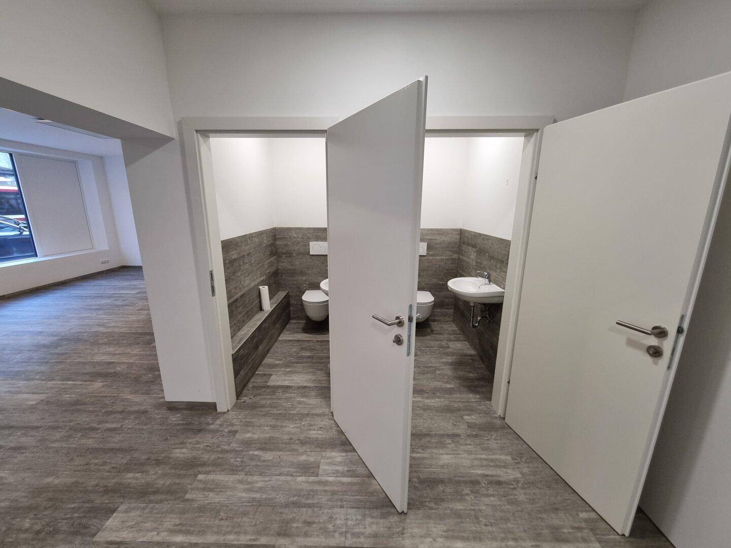 Zwei separate Toilettenräume mit Waschbecken und modernen Fliesen im unteren Bereich.