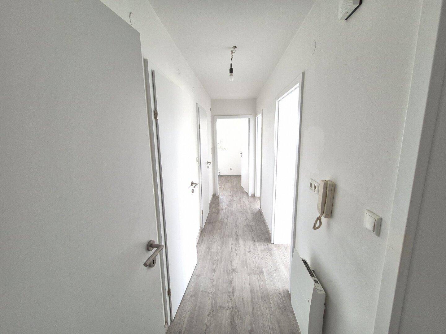 Heller Flur mit mehreren weißen Türen und modernem Laminatboden, der zu weiteren Räumen führt.