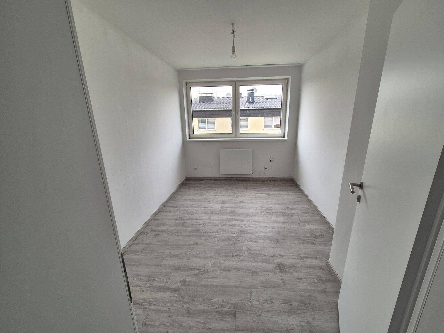 Helles Schlafzimmer mit Laminatboden und einem Fenster, das viel Tageslicht hereinlässt.