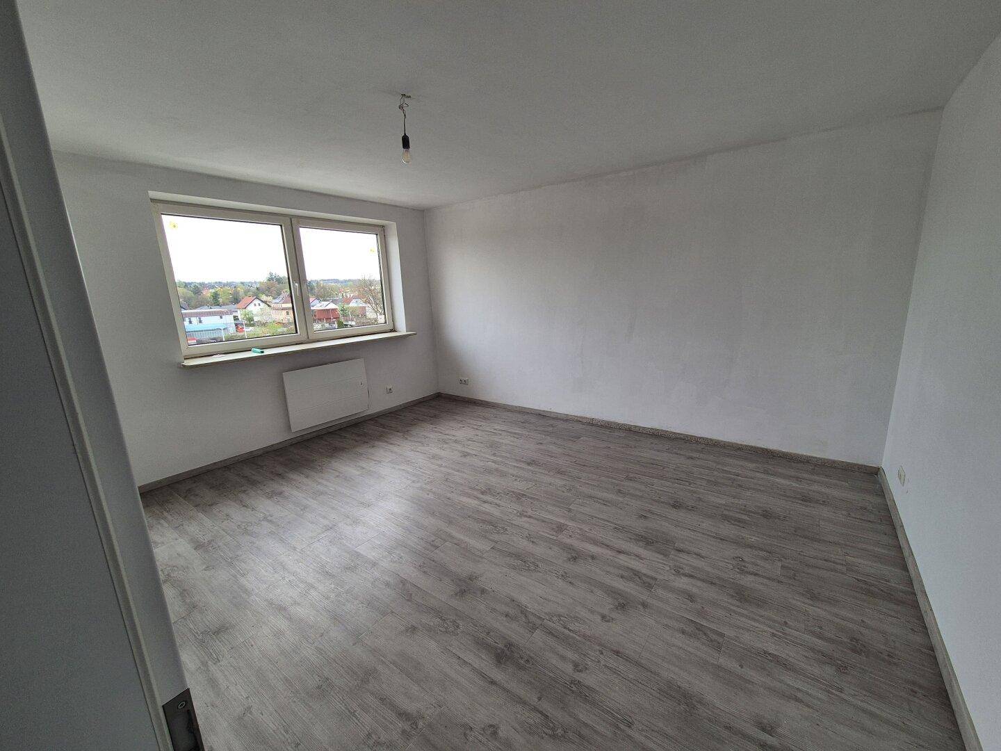 Geräumiges, helles Zimmer mit großen Fenstern und neuem Laminatboden, ideal als Wohnzimmer.
