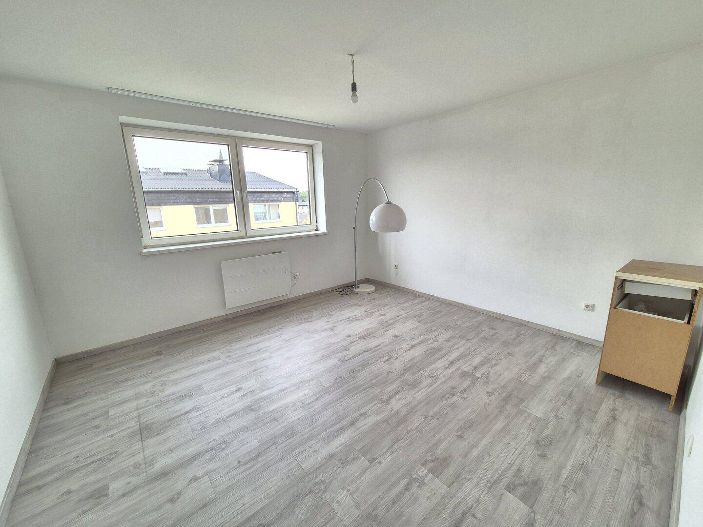 Lichtdurchflutetes Zimmer mit Laminatboden und einem Fenster, das eine angenehme Atmosphäre schafft.