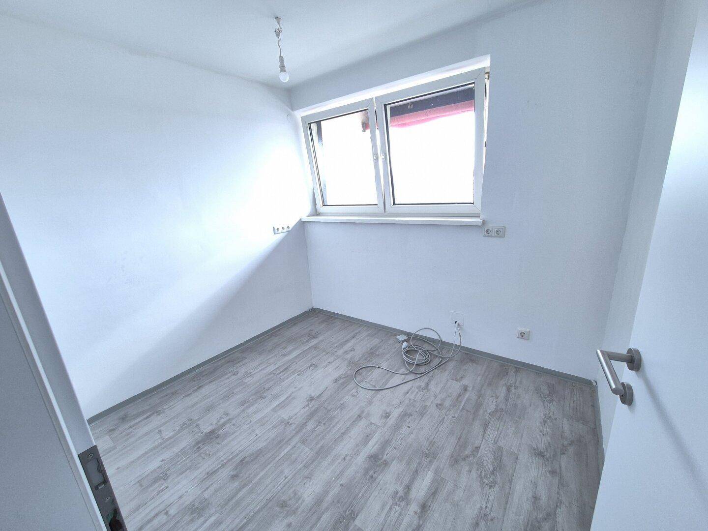 Kleines, helles Zimmer mit Laminatboden und Fenster, geeignet als Kinder- oder Arbeitszimmer.