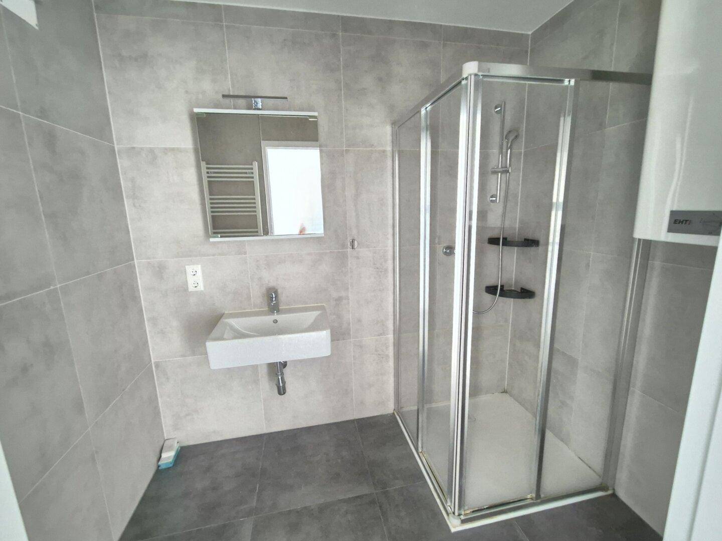 Modernes Badezimmer mit grauen Fliesen, Duschkabine und wandhängendem Waschbecken.