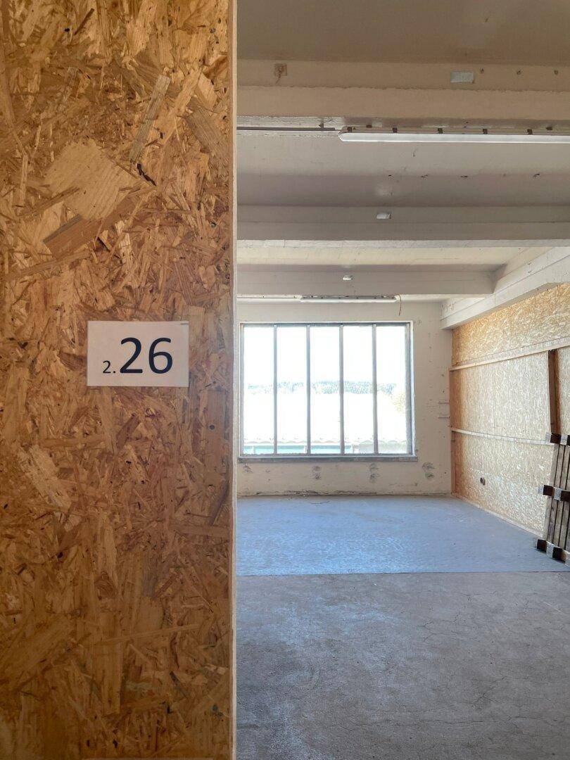 Blick in einen leeren Lagerraum mit OSB-Wänden, Betonboden und einem großen Fenster.