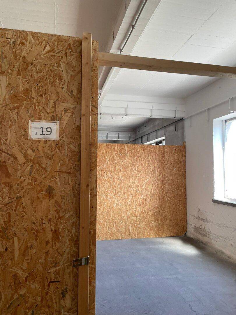 Leerer Lagerraum mit OSB-Wänden, Betonboden und einem Fenster, das Tageslicht hereinlässt.
