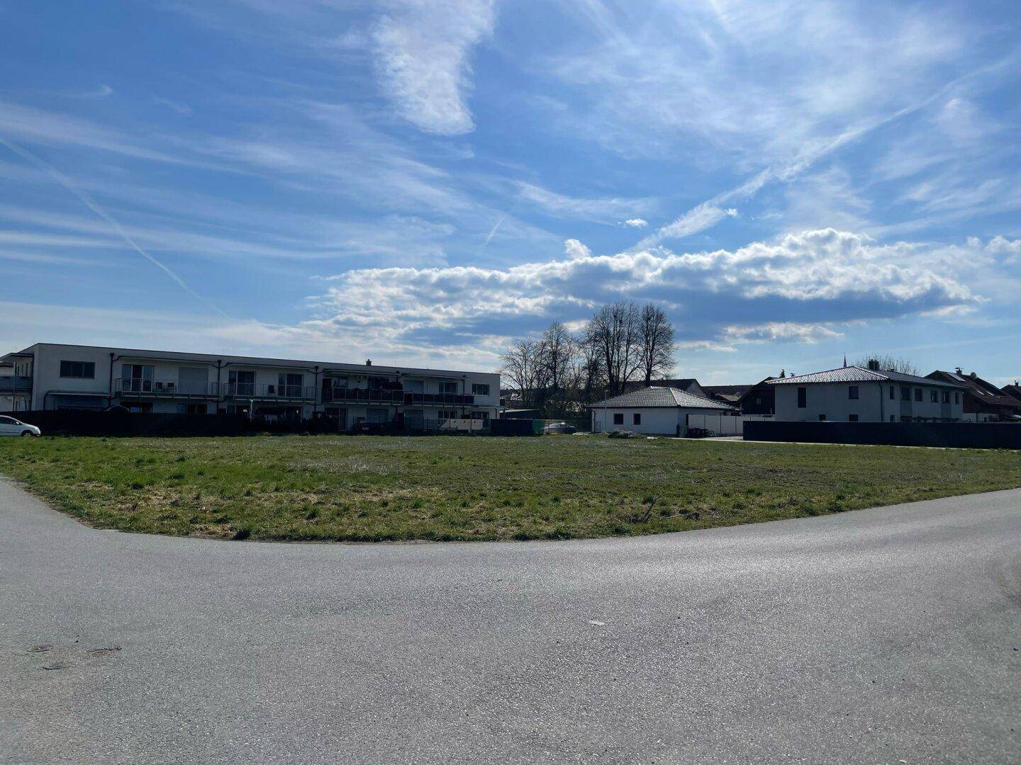 Offenes Feld mit Gras und Blick auf eine Reihe von Wohngebäuden und den blauen Himmel.