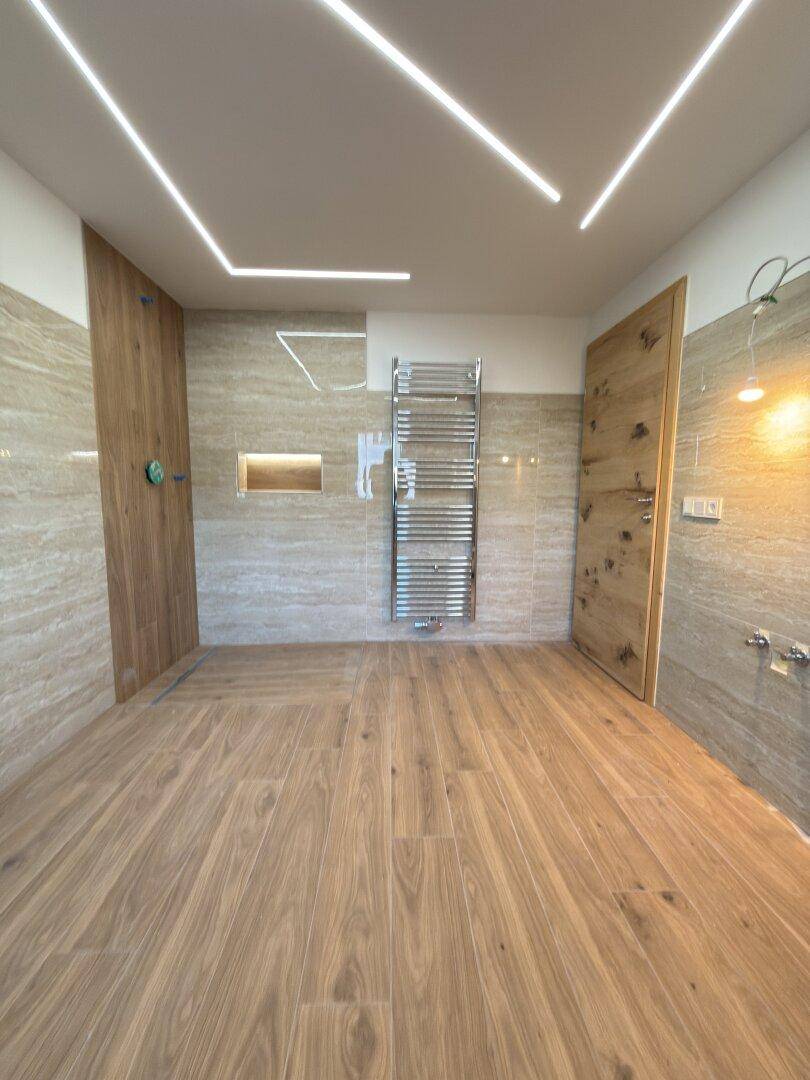 Modernes Badezimmer mit großformatigen Fliesen, Holztür und beheiztem Handtuchhalter.