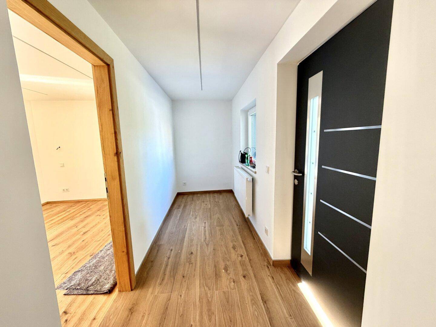 Heller Eingangsbereich mit Holzboden und moderner schwarzer Eingangstür.