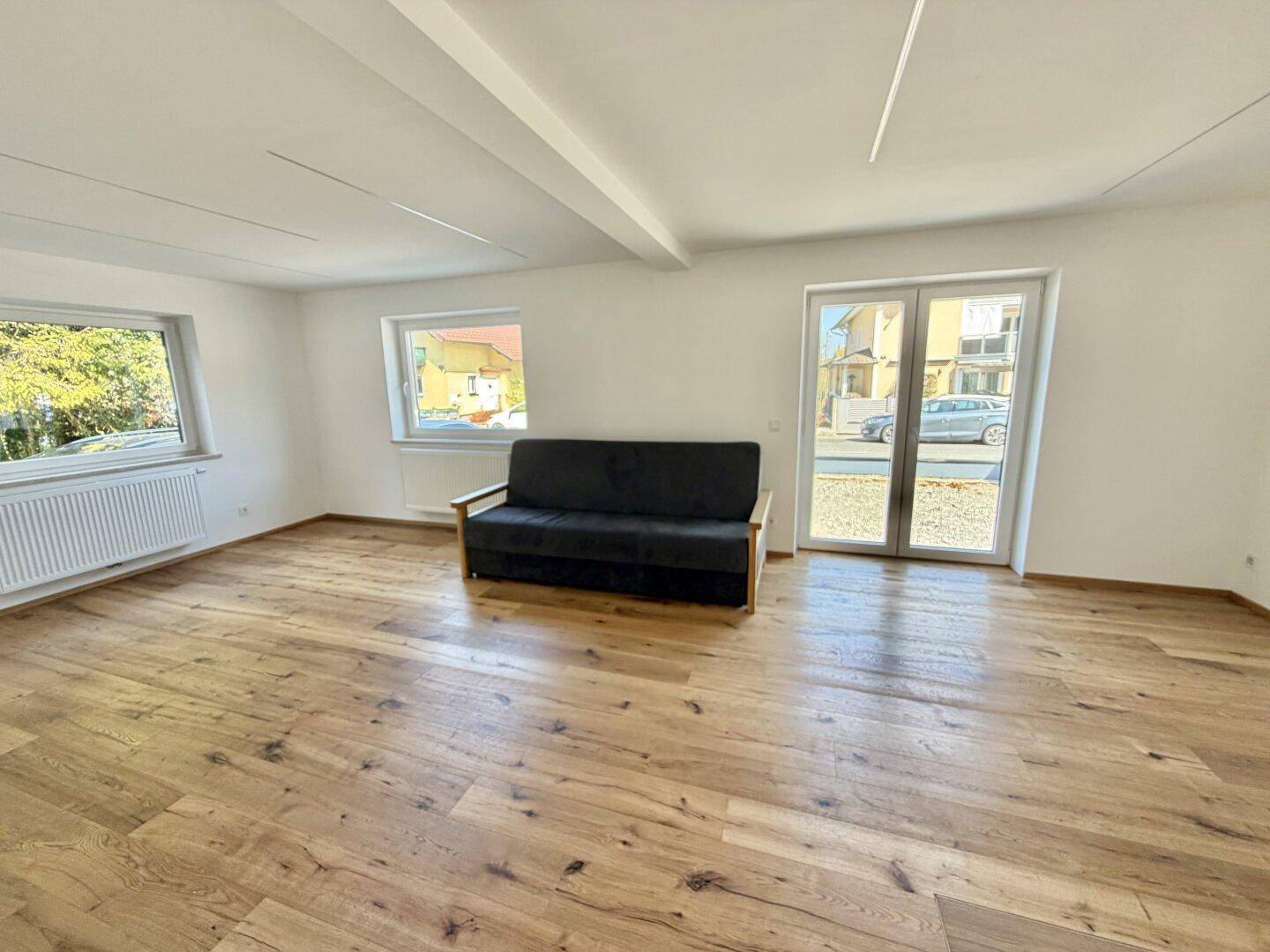 Helles Wohnzimmer mit Holzboden, großen Fenstern und Zugang zum Außenbereich.