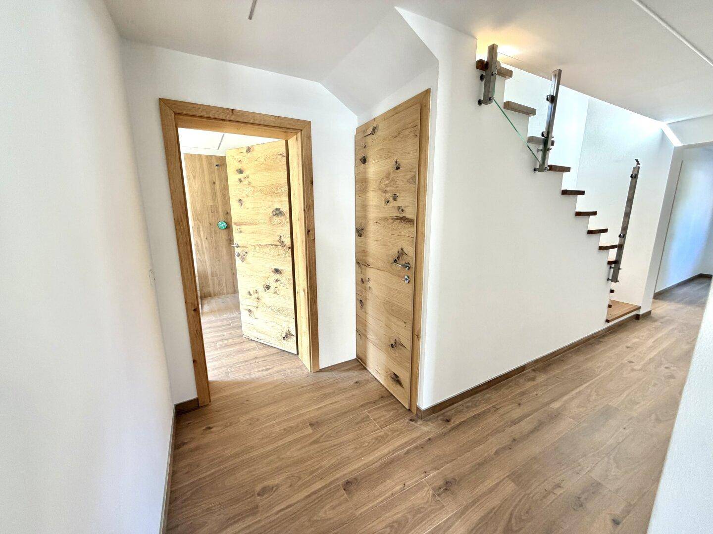 Flur mit Holztreppe und modernen Holztüren, die zu weiteren Räumen führen.