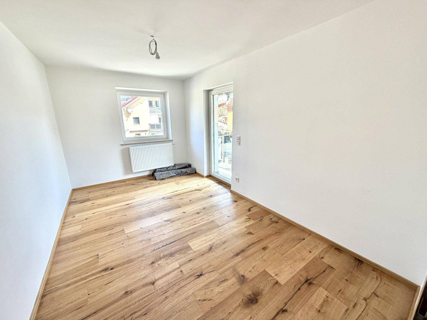 Helles Schlafzimmer mit Holzboden und Zugang zu einem Balkon oder einer Terrasse.