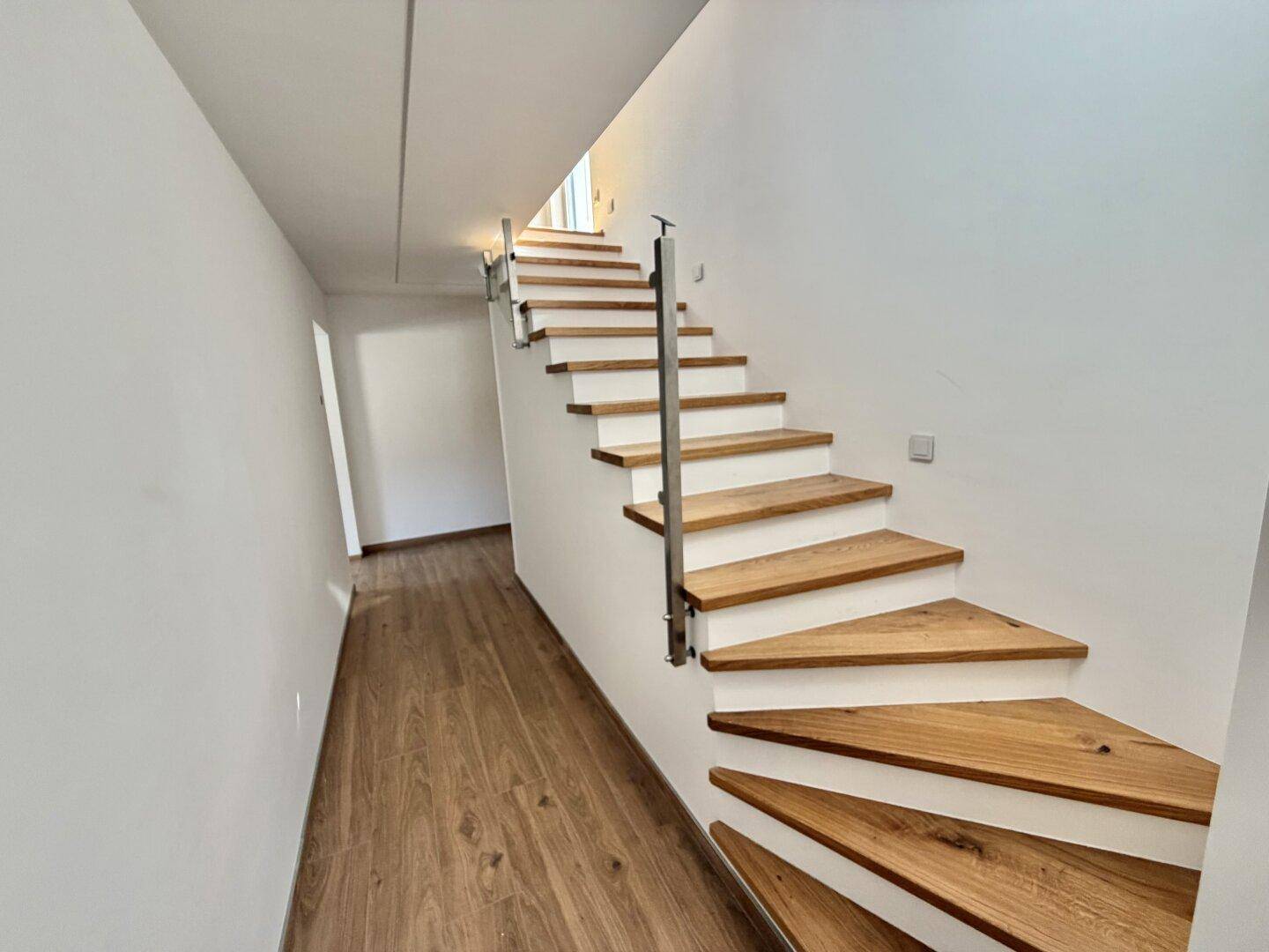Heller Flur mit offener Holztreppe und modernem Glasgeländer.
