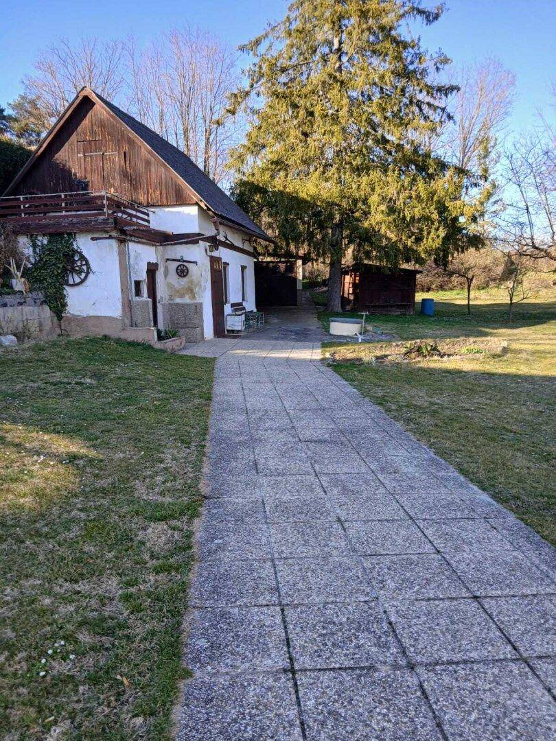Gepflasterter Weg führt durch den weitläufigen Garten zu einem rustikalen Nebengebäude.