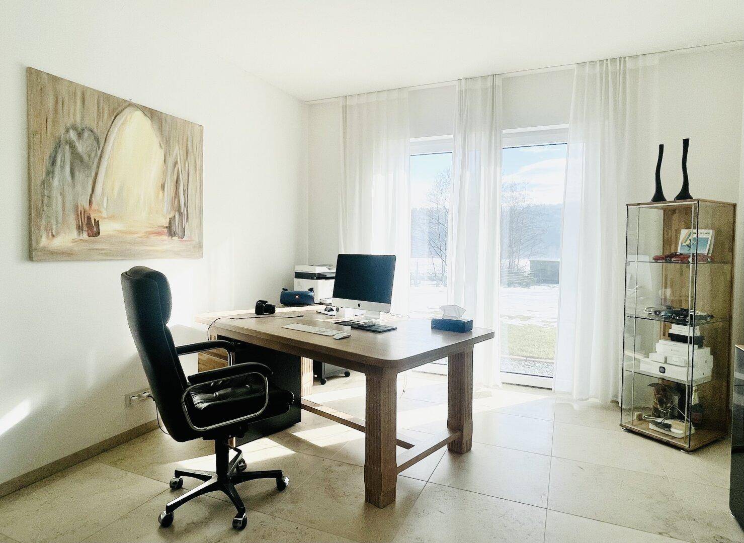 Helles Arbeitszimmer mit großem Schreibtisch, viel Tageslicht und Blick auf die Landschaft.