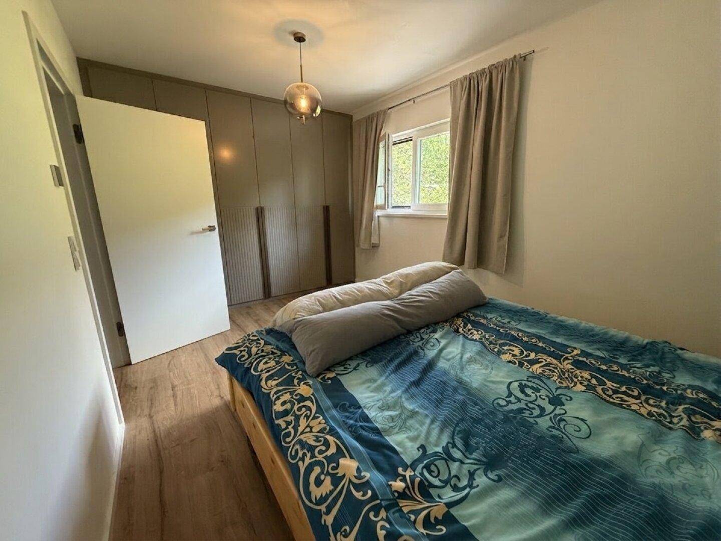 Gemütliches Schlafzimmer mit Holzboden, Einbauschränken und natürlichem Lichteinfall durch das Fenster.